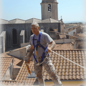 A roofer wearing a safety harness while working on a sloped roof, demonstrating the importance of maintenance and safety in extending a commercial roof’s lifespan.