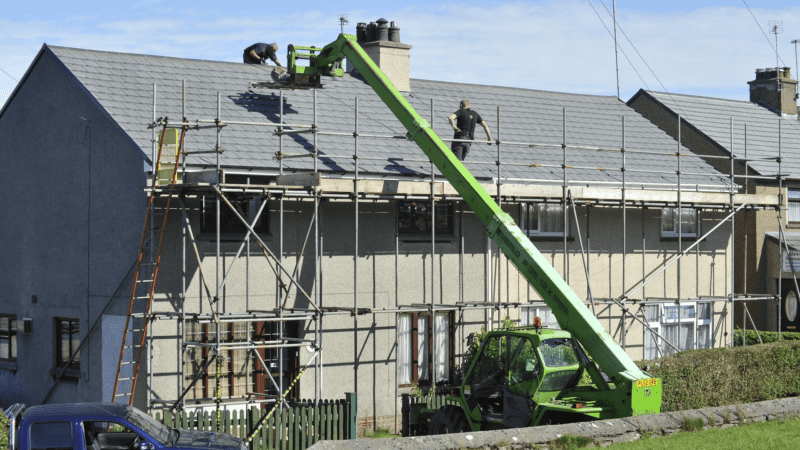 A professional roofing crew working on a large commercial building with scaffolding and safety gear, ensuring a longer-lasting roof.