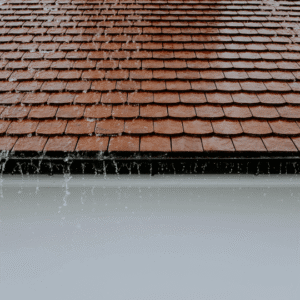 a close-up of a wet shingle roof with rainwater running off the edges, emphasizing the importance of sealing potential leaks before cooler temperatures cause further damage.