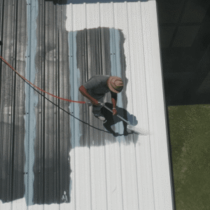 A worker applying a protective roof coating to a commercial metal roof to improve durability and energy efficiency.