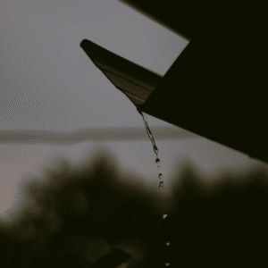 close-up of rainwater dripping from a gutter system, representing water management on flat roofs